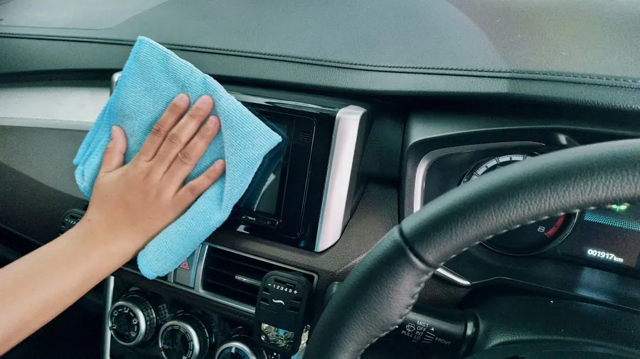 Hand wischt das Armaturenbrett neben dem Lenkrad mit einem blauen Mikrofasertuch ab