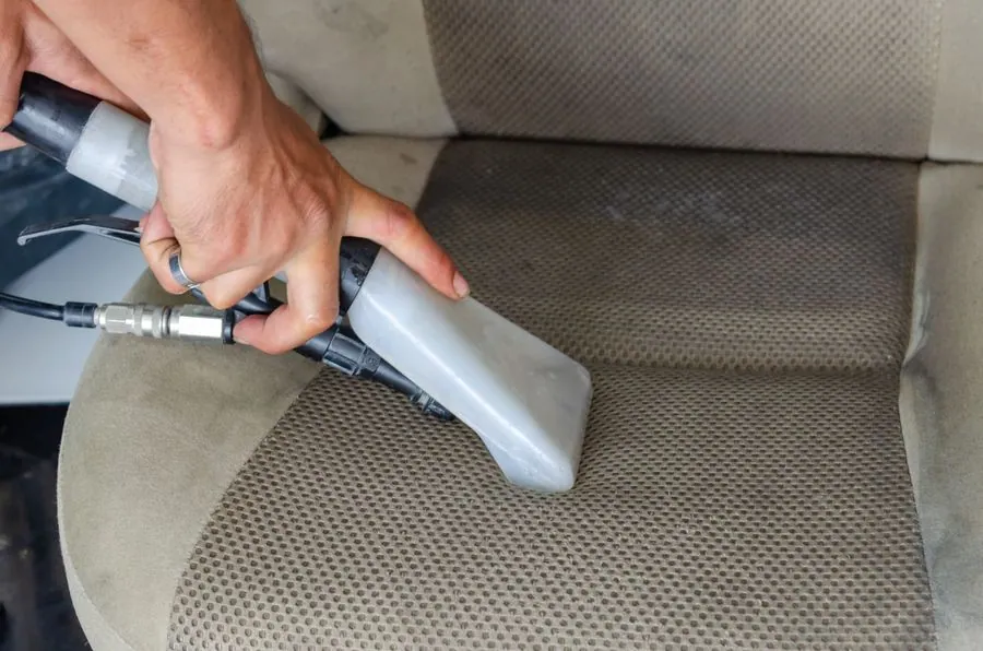 Hand führt die Düse eines Waschsaugers über einen verschmutzten Stoffsitz